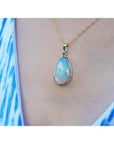 Ethiopian opal pendant with rainbow flashes in 14K yellow gold, worn on a blue and white patterned top.