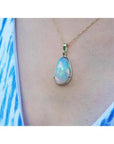 Ethiopian opal pendant with rainbow flashes in 14K yellow gold, worn on a blue and white patterned top.