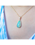 Opal pendant necklace on a person's neck wearing a blue and white patterned top.