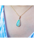Pear-shaped Ethiopian opal pendant with blue-violet play-of-color in 14K yellow gold on a woman's neck.