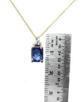 14k gold necklace with an emerald-cut blue sapphire pendant and three diamonds, next to a ruler.