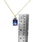 14k gold necklace with an emerald-cut blue sapphire pendant and three diamonds, next to a ruler.