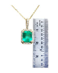 Emerald-cut Colombian emerald pendant with diamond halo on a gold chain, next to a ruler.