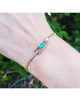 14K yellow gold bracelet with a central emerald-cut Colombian emerald flanked by diamond rows.