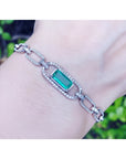 14K white gold paperclip bracelet with a vibrant emerald-cut emerald and diamond halo.