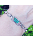 14K white gold paperclip bracelet with a vibrant emerald-cut emerald and diamond halo.
