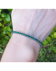 Natural Colombian emeralds tennis bracelet, 14K gold, round cut, medium deep green, on a wrist.