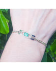 14K yellow gold bracelet with a rectangular Colombian emerald haloed by diamonds on a woman's wrist.