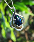 Silver pendant with a blue Ethiopian black opal against a green leafy background