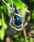 Silver pendant with a dark Welo opal teardrop against a blurred green background