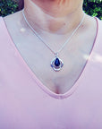 Person wearing a silver necklace with a teardrop black opal pendant outdoors