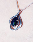 Silver pendant with a teardrop dark black opal on a light pink background