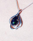 Silver pendant with a teardrop dark black opal on a light pink background