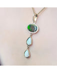 Black and white Australian opal pendant with an oval black opal, surrounded by diamonds, and two pear-shaped white opals, set in 14K yellow gold.