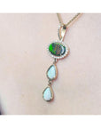 Black and white Australian opal pendant with an oval black opal, surrounded by diamonds, and two pear-shaped white opals, set in 14K yellow gold.