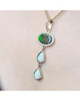 Black and white Australian opal pendant with an oval black opal, surrounded by diamonds, and two pear-shaped white opals, set in 14K yellow gold.