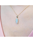Gold necklace with a natural opal pendant on a person's neck wearing a pink top.