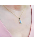 14K yellow gold necklace with a vibrant opal and diamond pendant on a woman's chest.