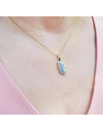 14K yellow gold necklace with a vibrant opal and diamond pendant on a woman's chest.