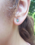 Pear-shaped opal doublet stud earring with red and blue play of colors, set in 14K yellow gold on an ear.