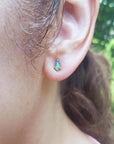 Pear-shaped opal doublet stud earring with red and blue play of colors, set in 14K yellow gold on an ear.