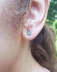 Pear-shaped opal doublet stud earring with red and blue play of colors, set in 14K yellow gold on an ear.