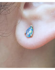 Pear-shaped opal doublet stud earring with red and blue play of colors, set in 14K yellow gold on an earlobe.