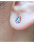 Pear-shaped opal doublet stud earring with red and blue play of colors, set in 14K yellow gold on an earlobe.