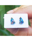 Teardrop-shaped opal earrings on a white card held by a hand with a blurred green background.