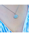 Necklace with an opal pendant worn by a person in a blue and white patterned top.
