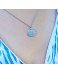Necklace with an opal pendant worn by a person in a blue and white patterned top.