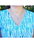 Person wearing a blue and white patterned top with a opal necklace outdoors.