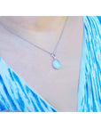 Teardrop-shaped opal pendant necklace worn by a person with a blue and white patterned garment.
