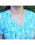 Person wearing a blue and white patterned top and opal pendant with a blurred green background.