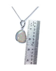 Opal pendant on a white gold chain with a ruler for scale on a white background