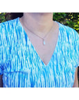 Pear-shaped white opal solitaire pendant in 14K white gold worn on a silver chain.