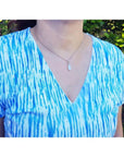 Pear-shaped white opal solitaire pendant in 14K white gold worn on a silver chain.