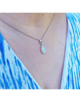 Pear-shaped white opal solitaire pendant in 14K white gold on a silver chain, worn on a person.