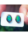 Opal earrings held on a white card between fingers.