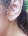 Oval blue Australian opal doublet stud earring in 14k yellow gold, bezel set on an ear.