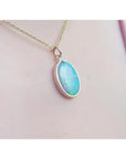 Oval Australian opal pendant with green-bluish hues in a 14K yellow gold setting on a chain.