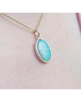 Oval Australian opal pendant with green-bluish hues in a 14K yellow gold setting on a chain.