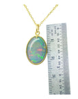 Opal pendant necklace with gold chain next to a ruler for scale on a white background