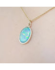 Oval Australian opal pendant with green-bluish rainbow play, set in 14K yellow gold on a chain.
