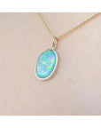 Oval Australian opal pendant with green-bluish rainbow play, set in 14K yellow gold on a chain.
