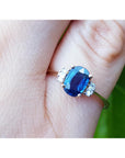 Blue sapphire ring with side diamonds on a hand against a blurred green background