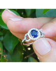 1.08 ct oval blue sapphire ring in 14K white gold with diamond halo, held by fingers.