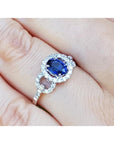 1.08 ct oval blue sapphire ring with diamond halo and 14K white gold band on a finger.