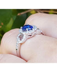 1.08 ct oval blue sapphire ring in 14K white gold with diamond halo on a finger.