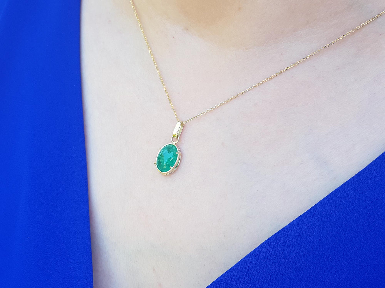 Gold necklace with an emerald pendant on a person wearing a blue and white outfit.